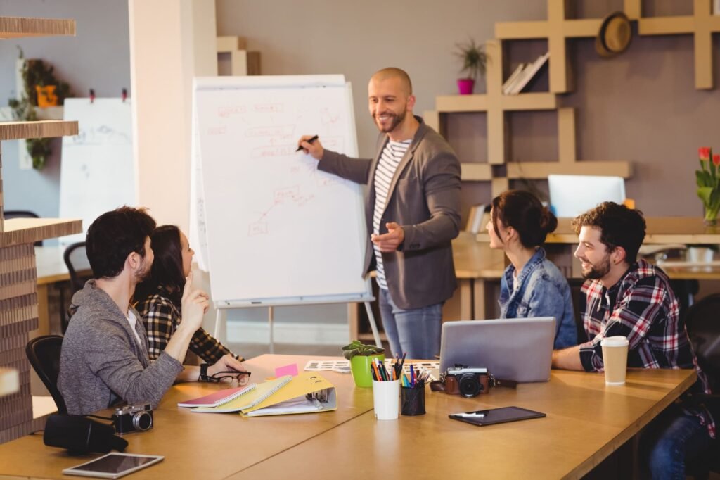A team gathering around a table as a colleague presents ideas on a whiteboard